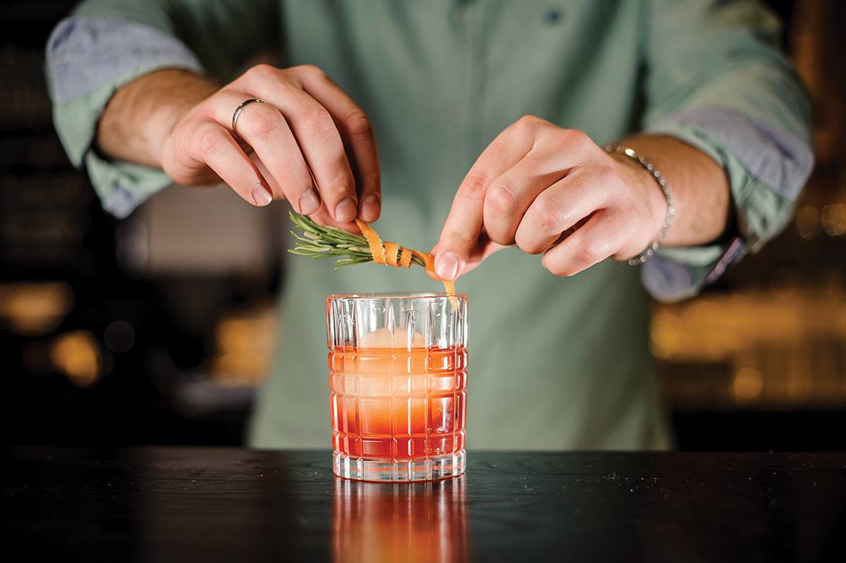 Bartender decorates cocktail with orange peel and rosemary