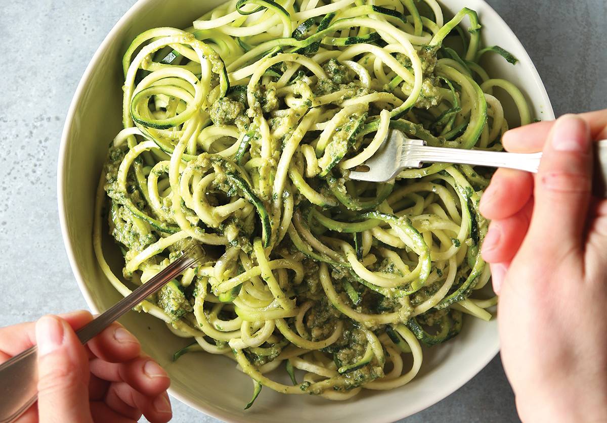 Female hands mixing zucchini noodles with pesto sauce