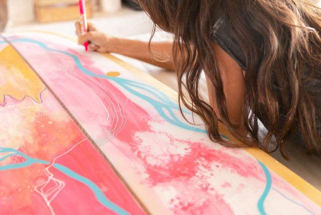 Artist Natalie Brake painting a surfboard.