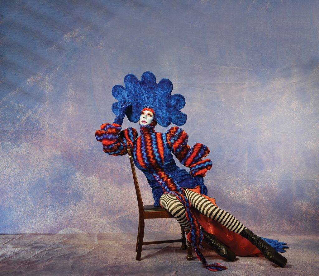 Victoria-based drag queen JIMBO poses in costume on a chair.