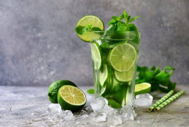 Summer citrus lemonade mojito in a tall glass on a grey slate, stone or concrete background.