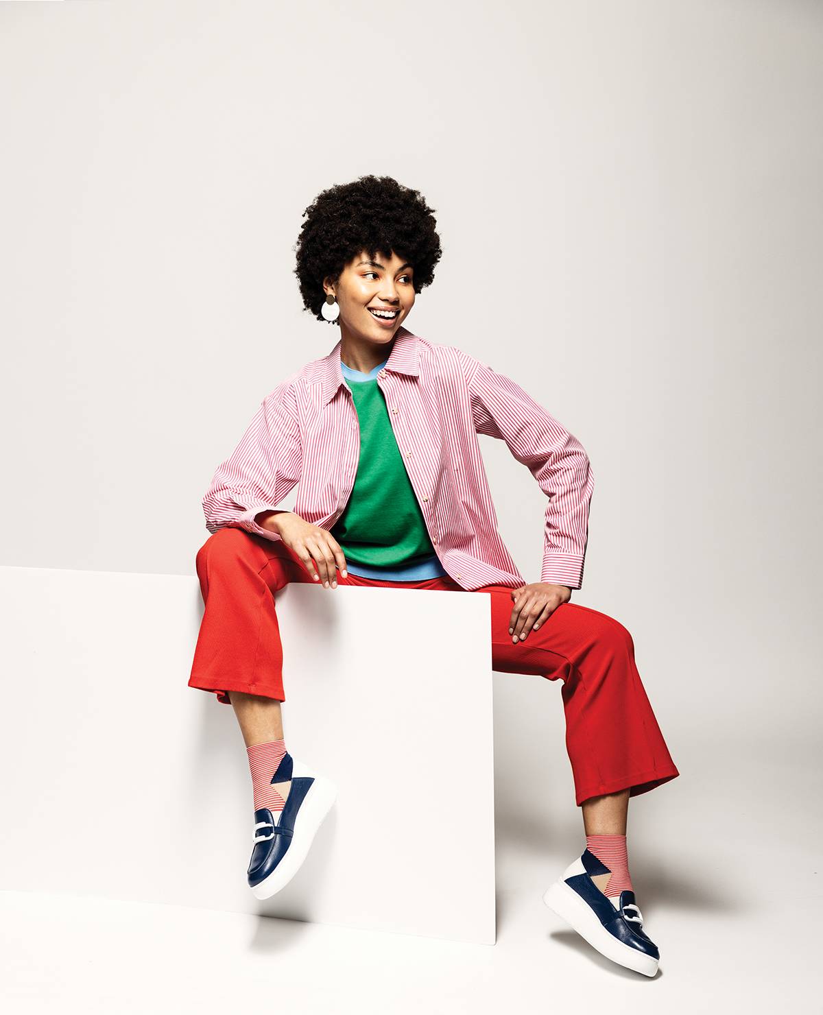 Pop striped button-up shirt and Rib Kick Flare trouser in tomato, both by DONNI, available at Still Life Boutique. Green Vitex Uni Tee by Our Sister, available at Still Life Boutique. Ping Pong sporty short crew socks by Hansel from Basel available at De Mode En Vogue. Blue and white Wonders Basille loafers, available at Waterlily Shoes. Earrings, stylist’s own.
